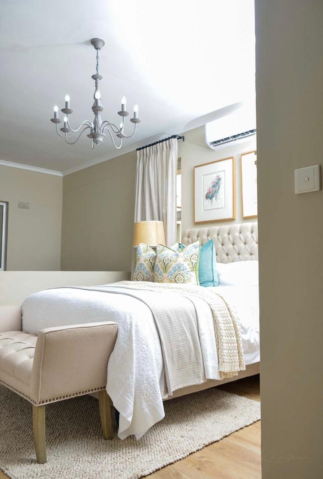 The bedroom at dusk, with a chandelier and the air-conditioning unit